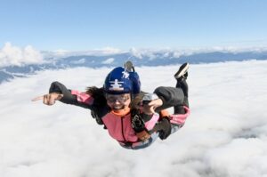 Paraquedista de capacete azul e macacão rosa em queda livre sobre as nuvens